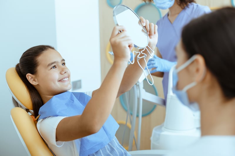 happy-girl-in-dental-chair-with-napkin-looks-in-mi-3JFR483-2